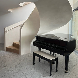 Spiral staircase with a black piano and bench in a modern interior setting.
