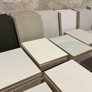 Stacks of white and gray tiles against a textured wall.