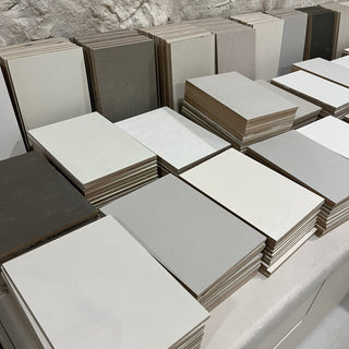 Stacks of ceramic tiles in various shades of gray and beige plaster on a stone surface.